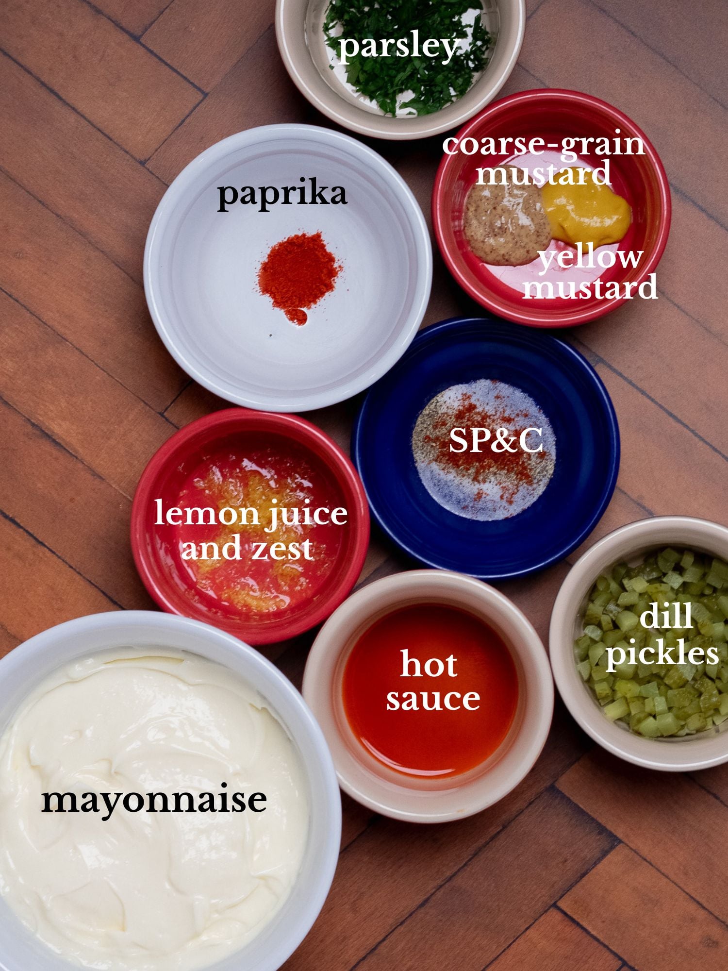 Ingredients for Cajun tartar sauce in bowls on a dark brown wooden background.