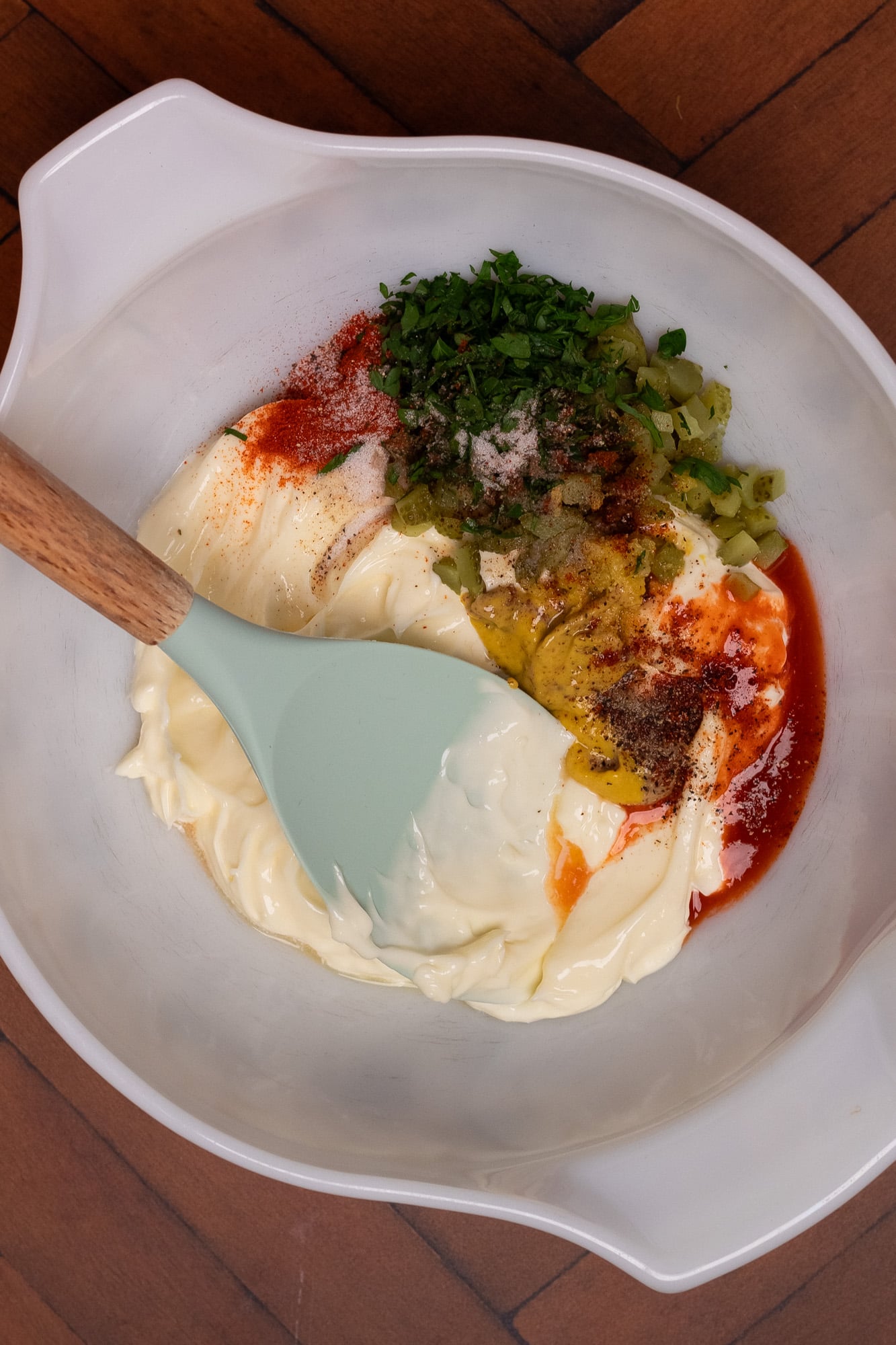 Mayonnaise, two types of mustards, parsley, pickles, hot sauce, lemon juice, and lemon zest in a white vintage Pyrex bowl.
