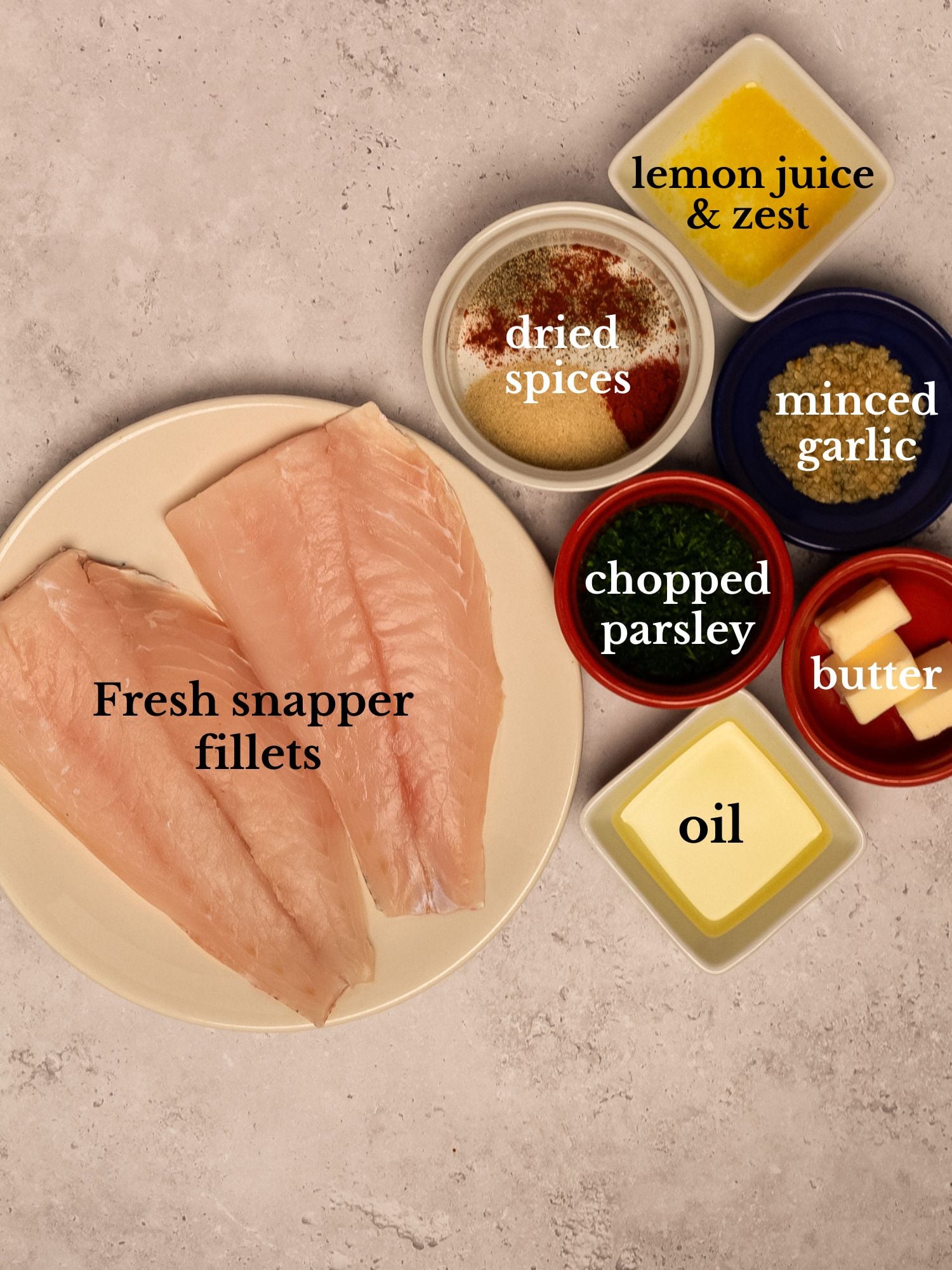 Ingredients for pan seared snapper in bowls on a white marbled background.