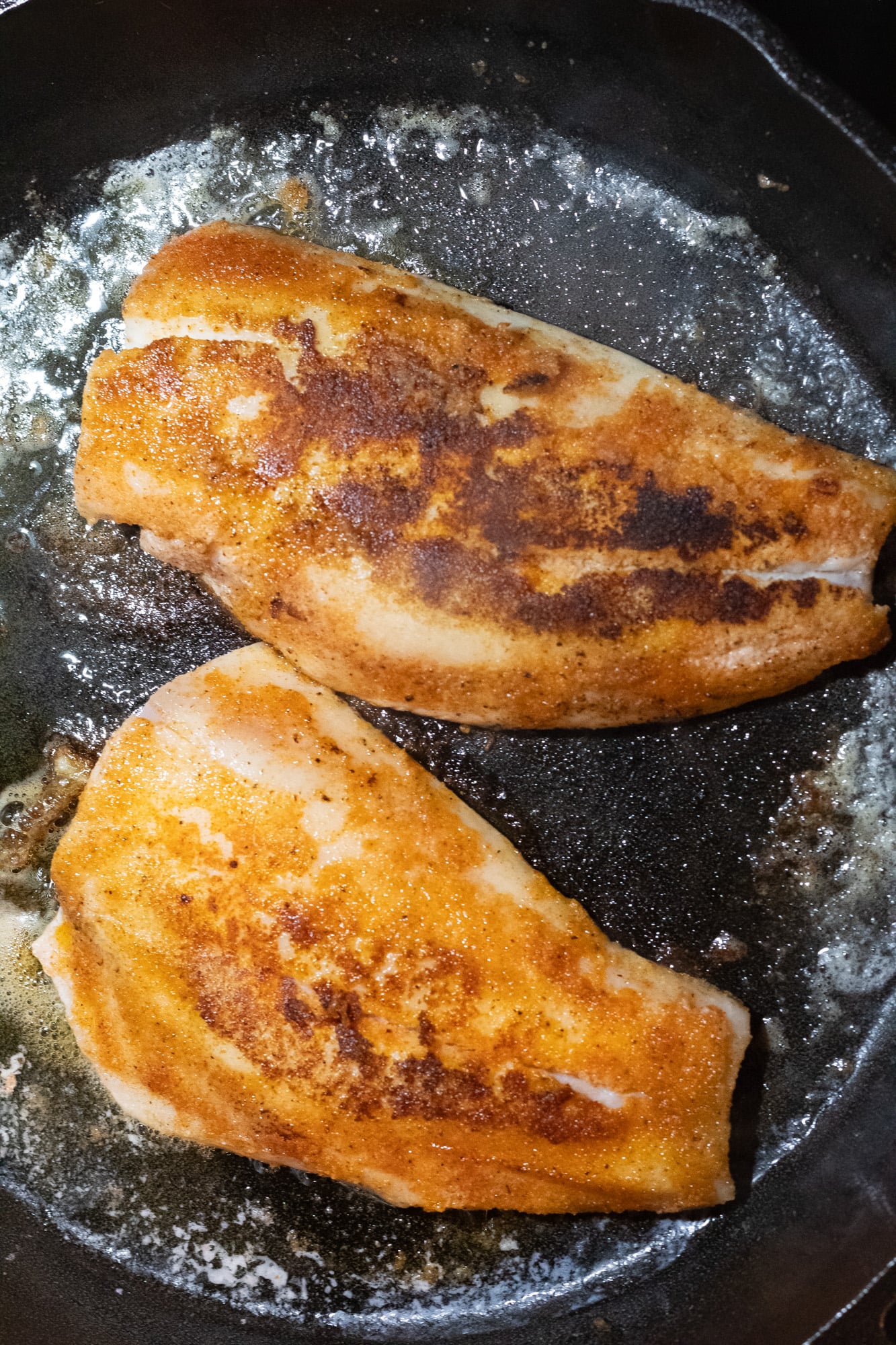 Two fish fillets cooking in brown butter.