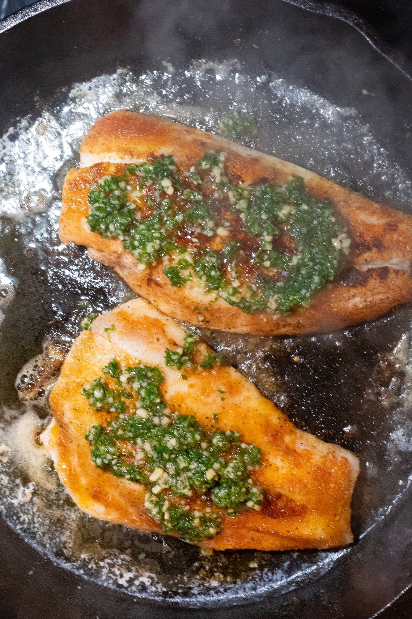 Sauce on top of pan-seared snapper in a pan.