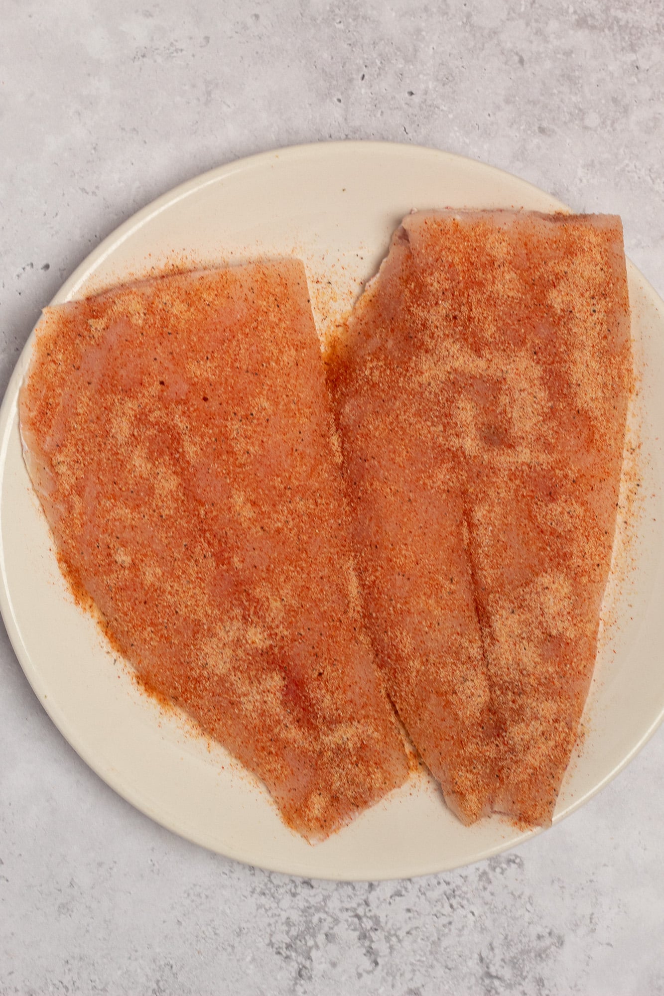 Two fresh red snapper fillets covered with dried spices on a plate.