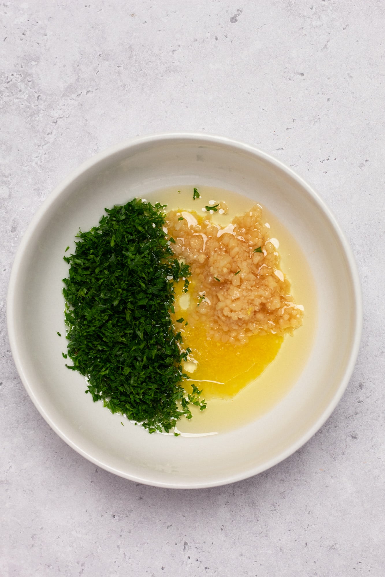 Garlic, parsley, lemon juice, and olive oil in a small white bowl.