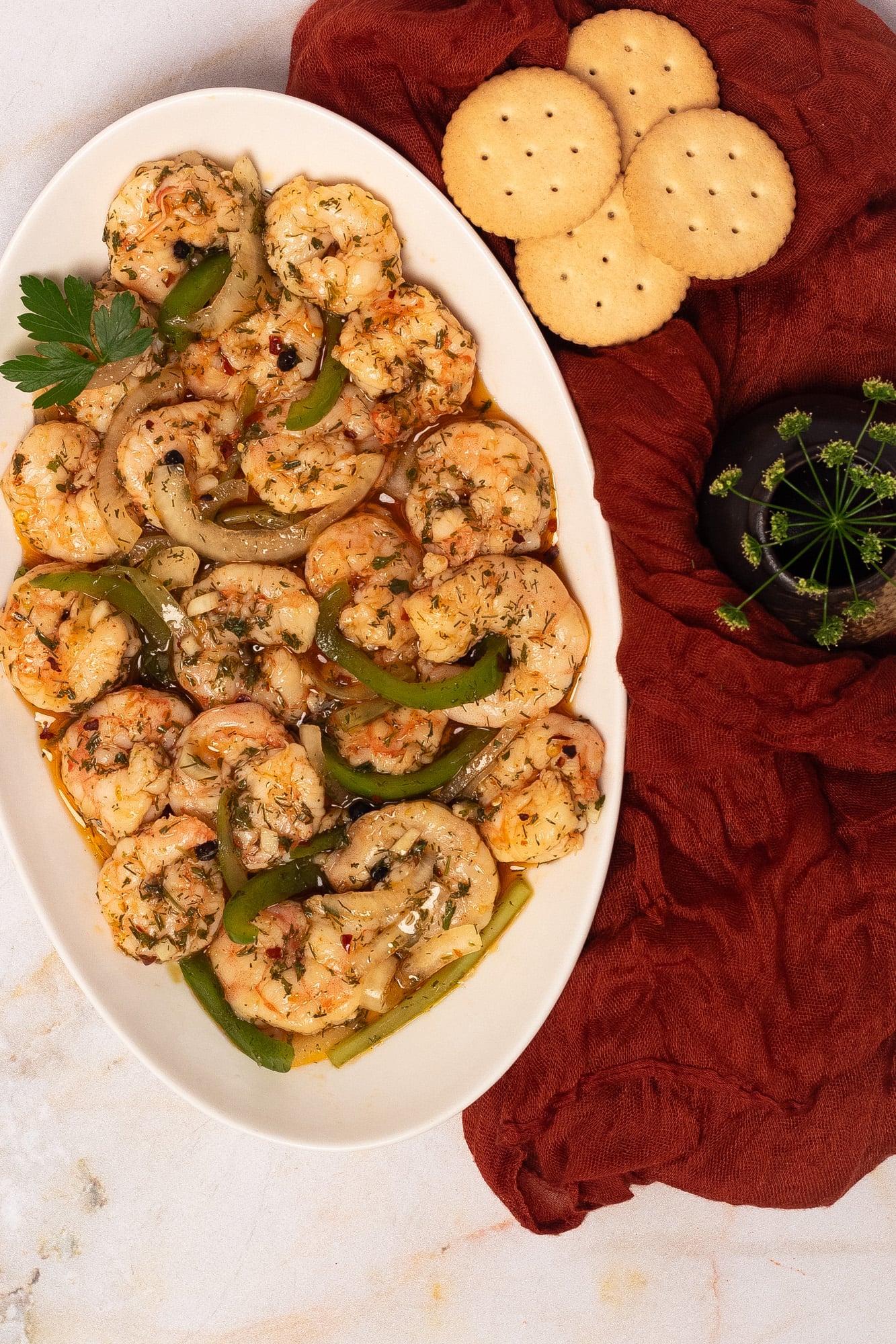 A white oval platter topped with pickled shrimp with finely sliced onions, green bell peppers, and celery ribs.