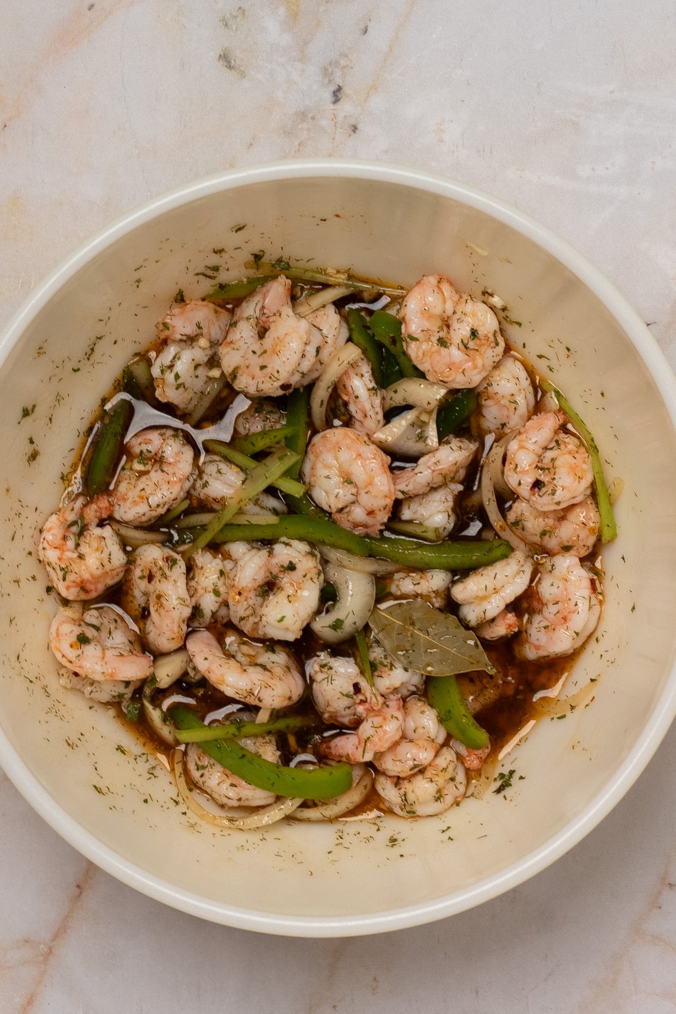 Cooked shrimp stirred into a pickling brine in a large yellow vintage Pyrex bowl.