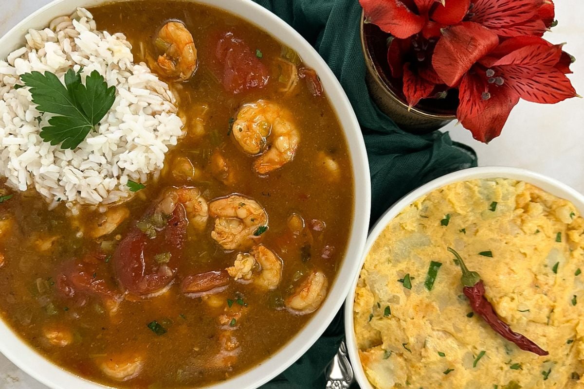 Shrimp etouffee with rice on top alongside a green napkin, potato salad, and a red flower.