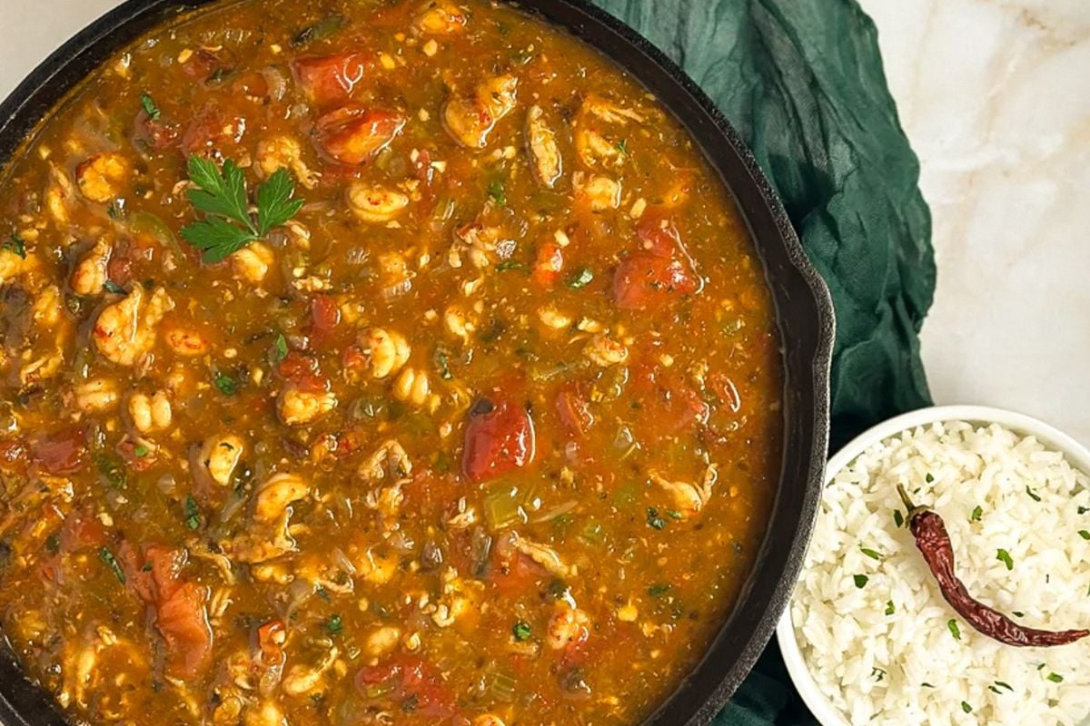Crawfish etouffee in a black cast iron skillet alongside a dark green napkin and small bowl of rice.