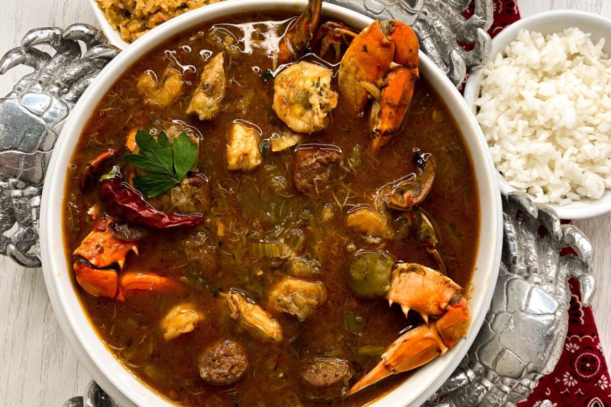 Creole gumbo in a round white bowl on top of a decorative silvertone serving platter with silver crabs on each corner.