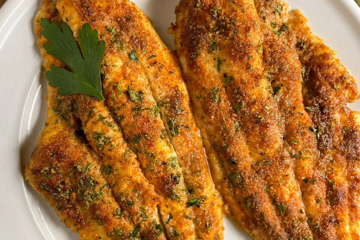 Two Cajun baked catfish fillets on a round white plate.