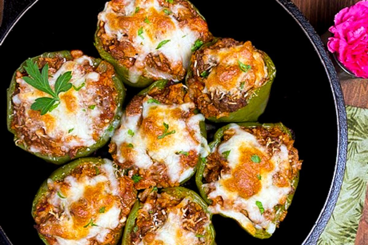 Cajun stuffed bell peppers in a cast iron skillet alongside a green napkin and pink flower.