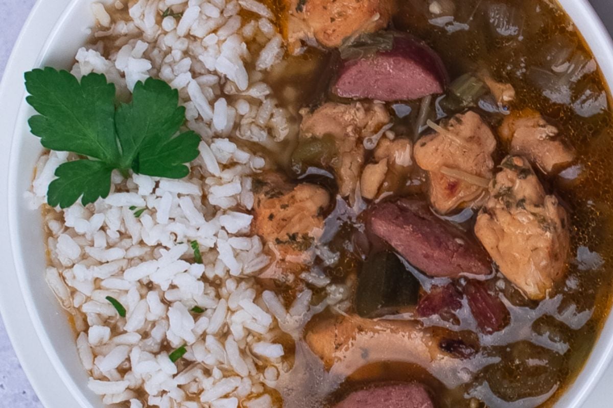 Chicken and sausage gumbo with rice on top and a whole parsley leaf garnish.