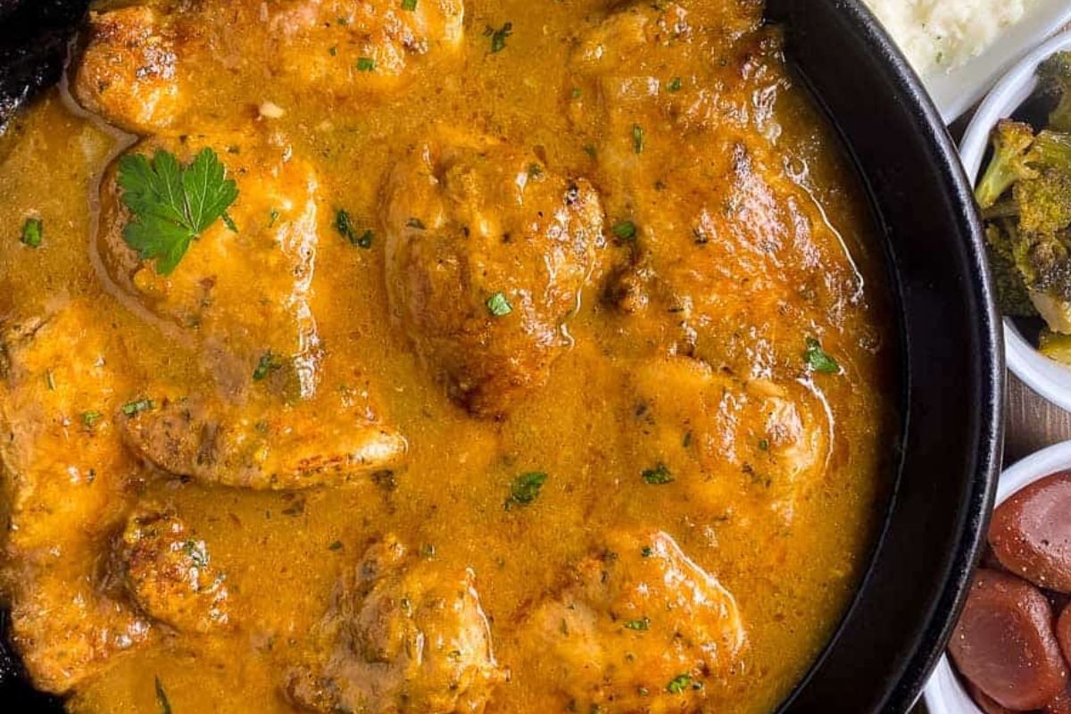 A closeup image of Cajun smothered chicken with brown gravy in a cast iron skillet with a whole parsley leaf garnish.