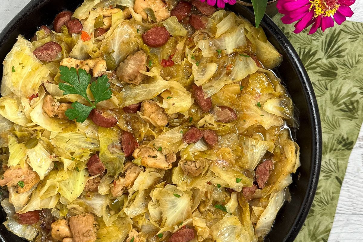 Cajun smothered cabbage with chicken and sausage in a black cast iron skillet.