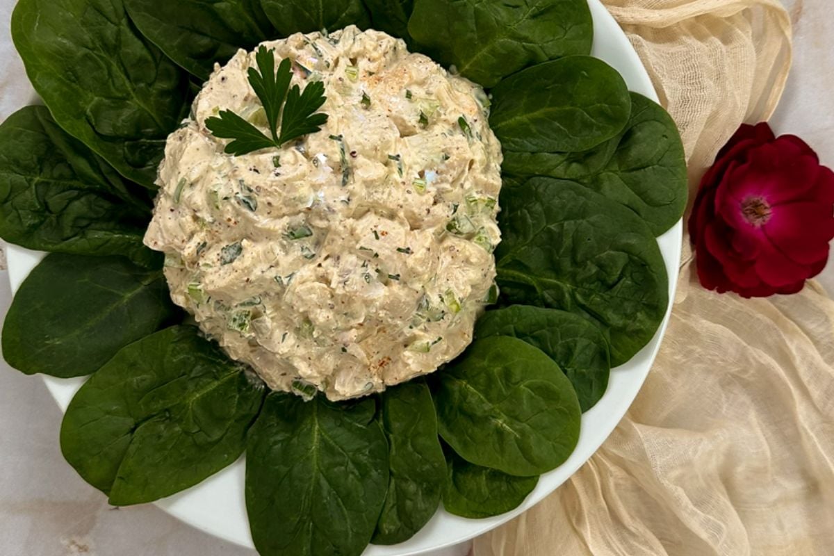 Cajun chicken salad in the middle of fresh spinach leaves with a whole parsley leaf garnish on a round white plate. 