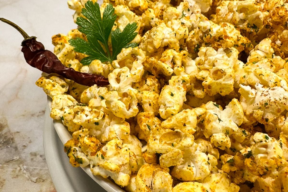 Cajun popcorn in a white bowl with a whole parsley leaf and whole cayenne pepper garnish. 