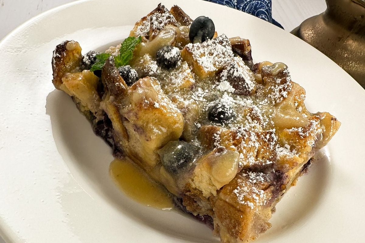 A closeup of a Louisiana blueberry bread pudding slice on a round white plate. 