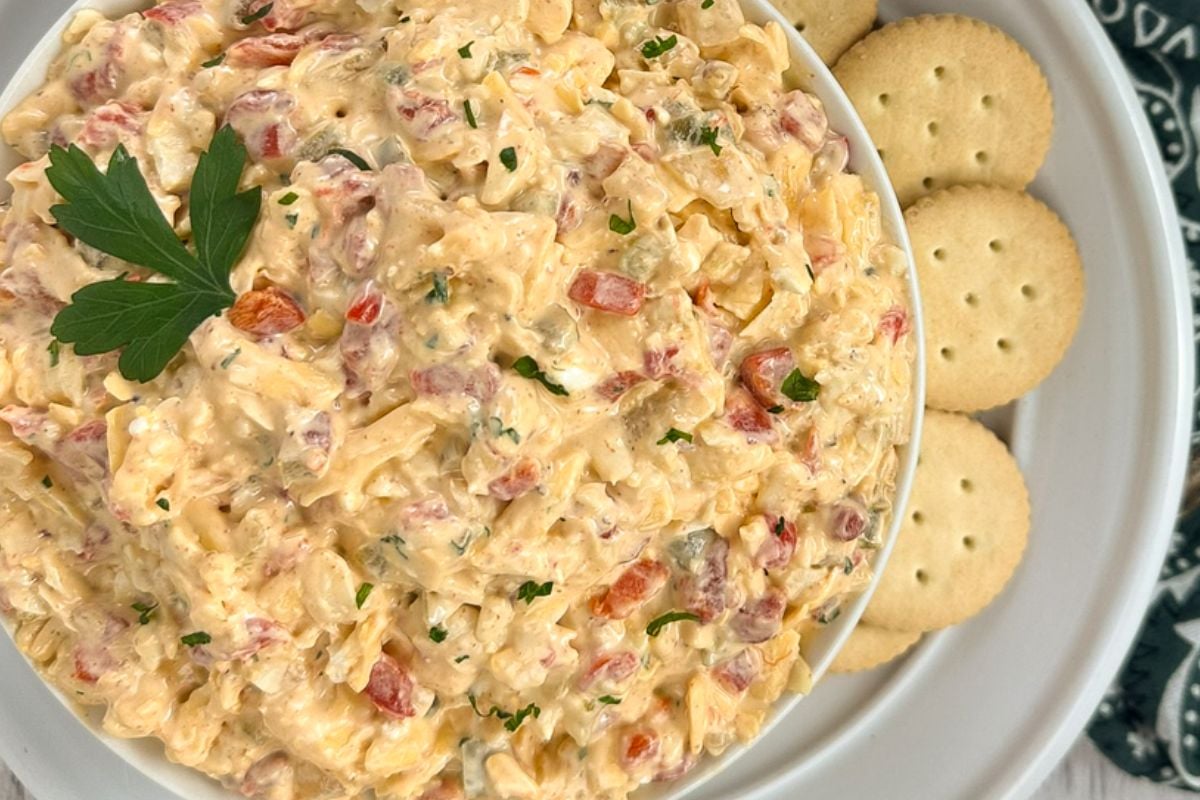 Cajun pimento cheese in a round white bowl alongside crackers. 
