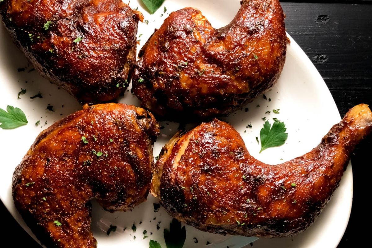 Oven-smoked chicken leg quarters on an oval white plate. 