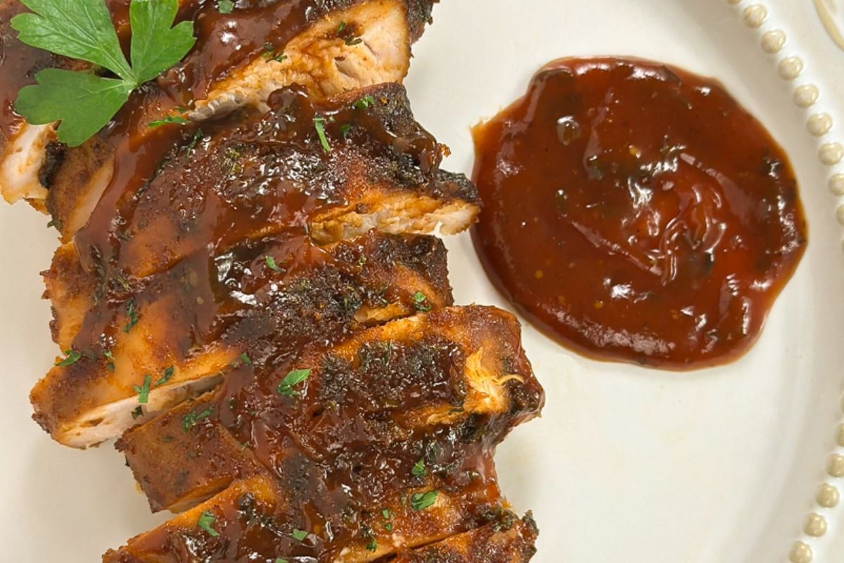 A sliced smoked chicken breast on a round white plate. 