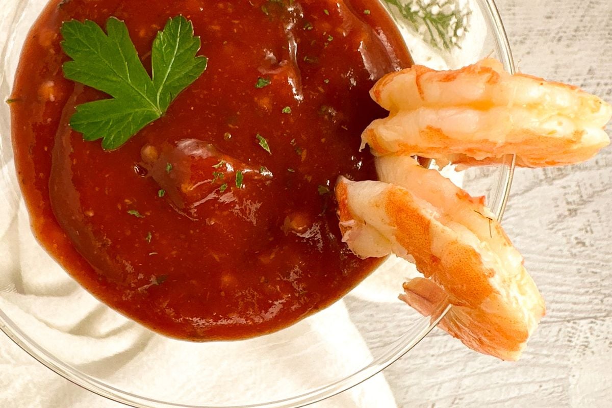 Cajun cocktail sauce in a martini glass with two shrimp on the side of the glass. 