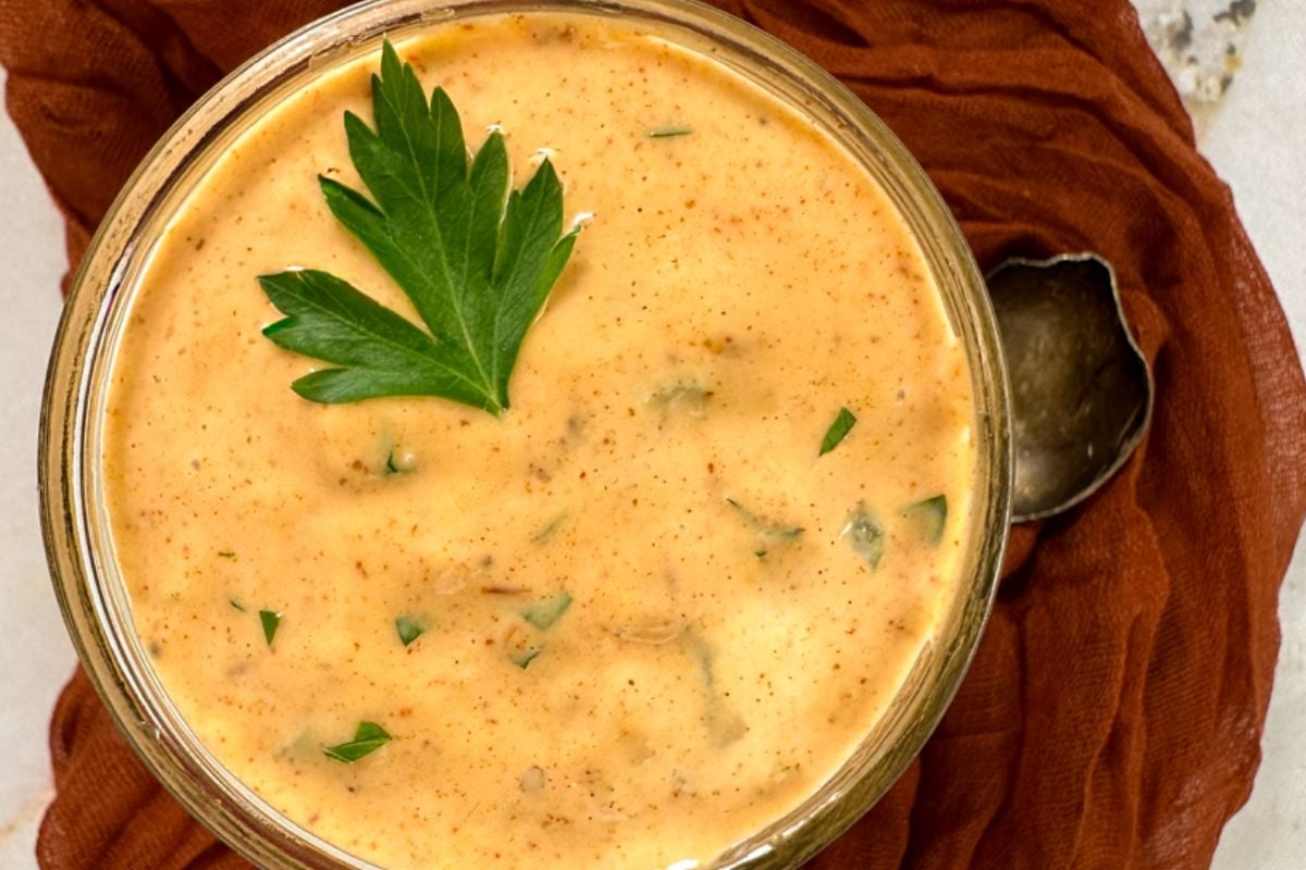 Louisiana remoulade sauce in small glass jar alongside a rust-colored napkin and a small spoon.