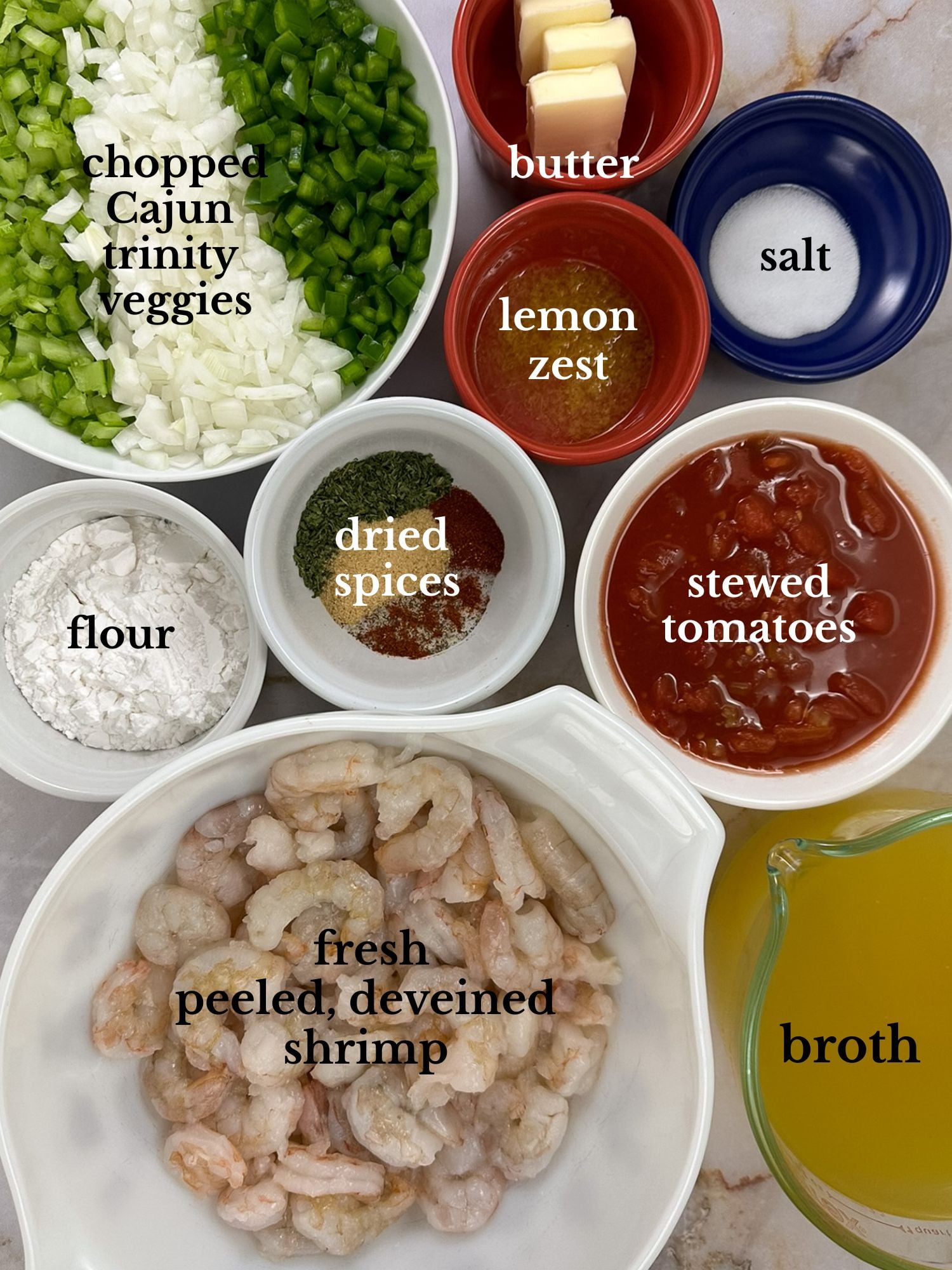 Ingredients for shrimp etouffee in bowls on a white marbled background.