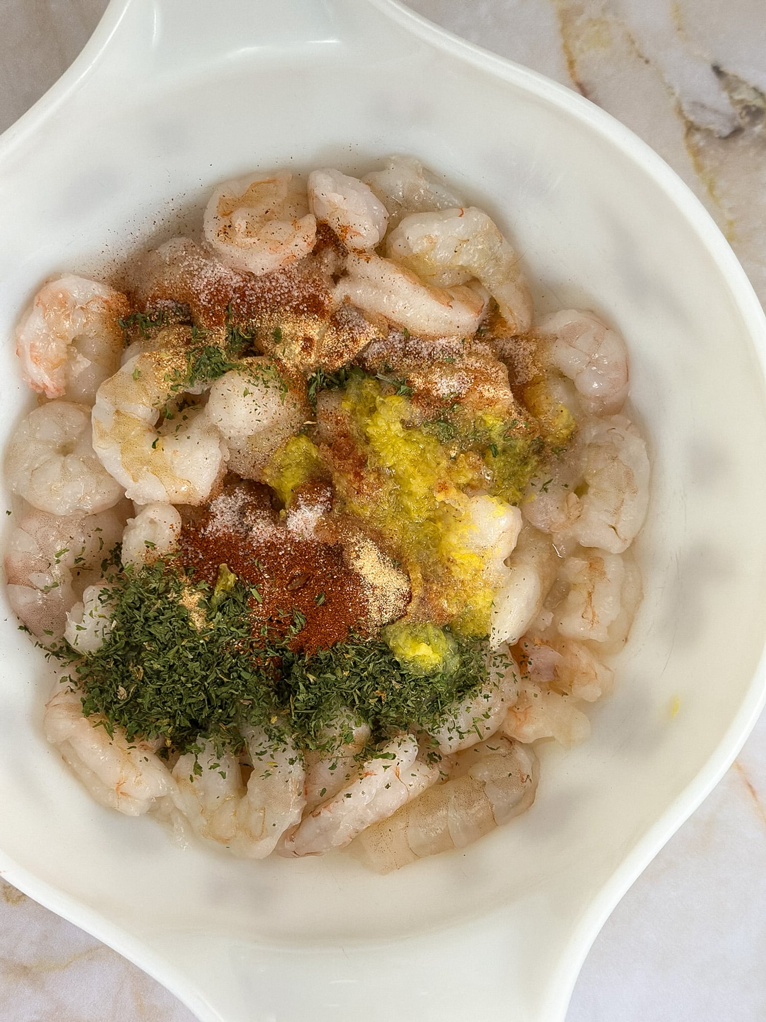 Dried seasonings and lemon zest over fresh shrimp in a bowl.
