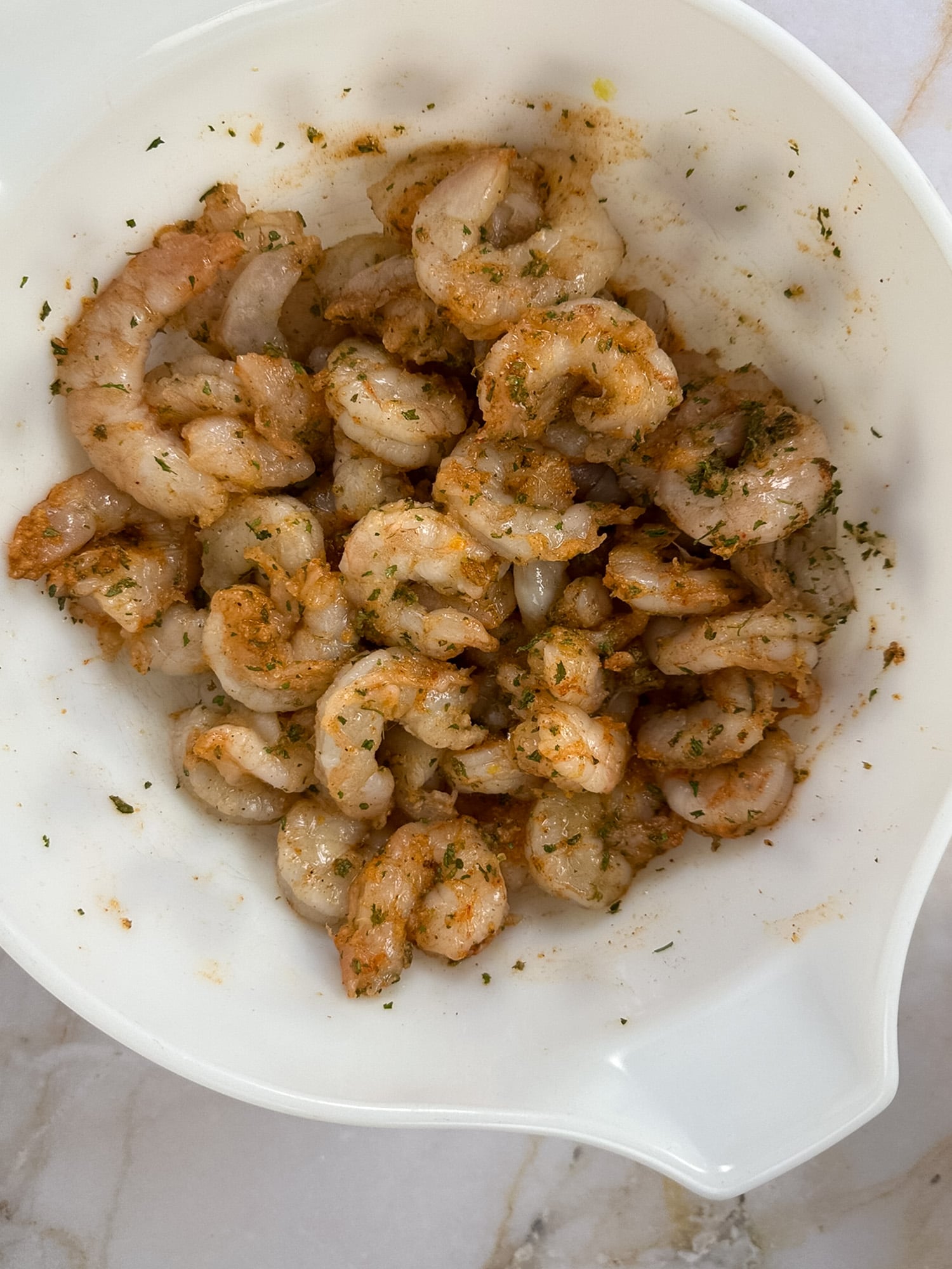 Seasoned shrimp in a vintage white mixing bowl.