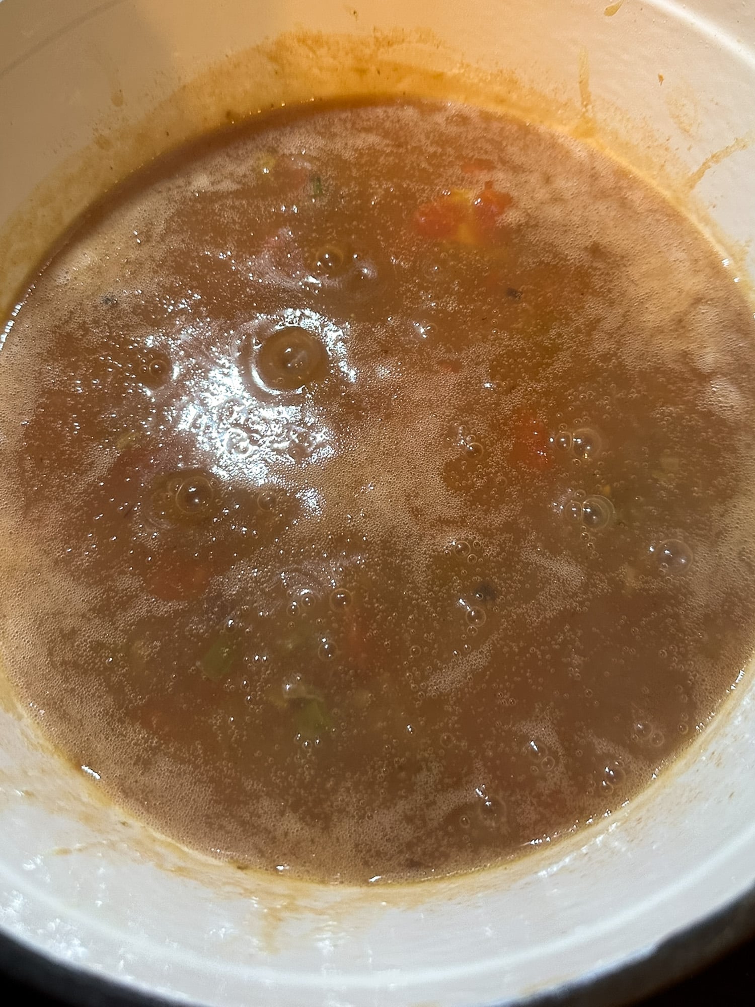 Stewed tomatoes stirred into a dark brown roux in a pot.
