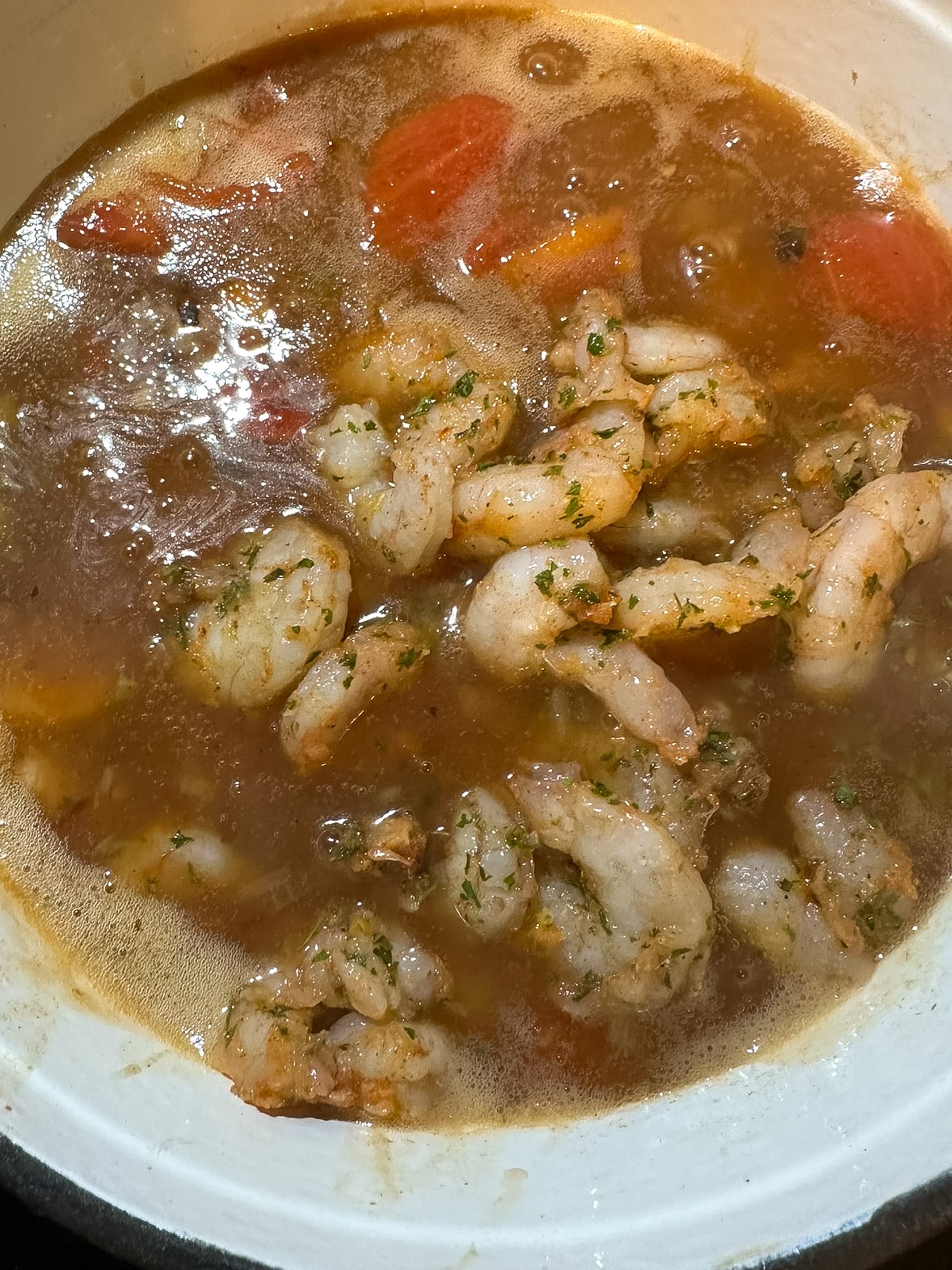 Raw seasoned shrimp over a tomatoey, roux-based gravy in a pot.