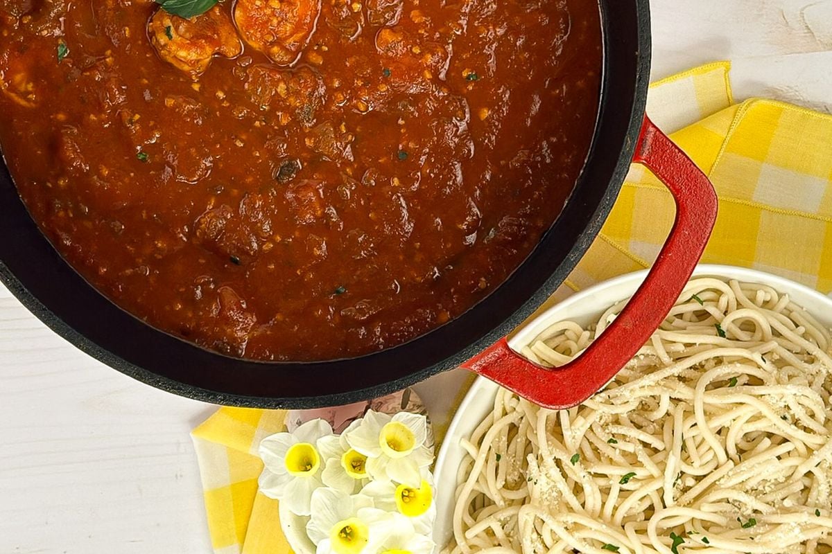 Cajun shrimp spaghetti alongside white flowers and a yellow and white napkin. 