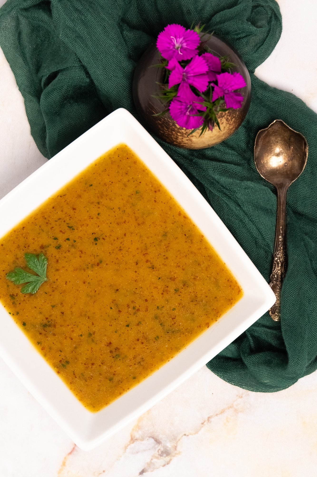 Creole mustard vinaigrette in a square white bowl with a green napkin, purple flowers, and an antique golden spoon.