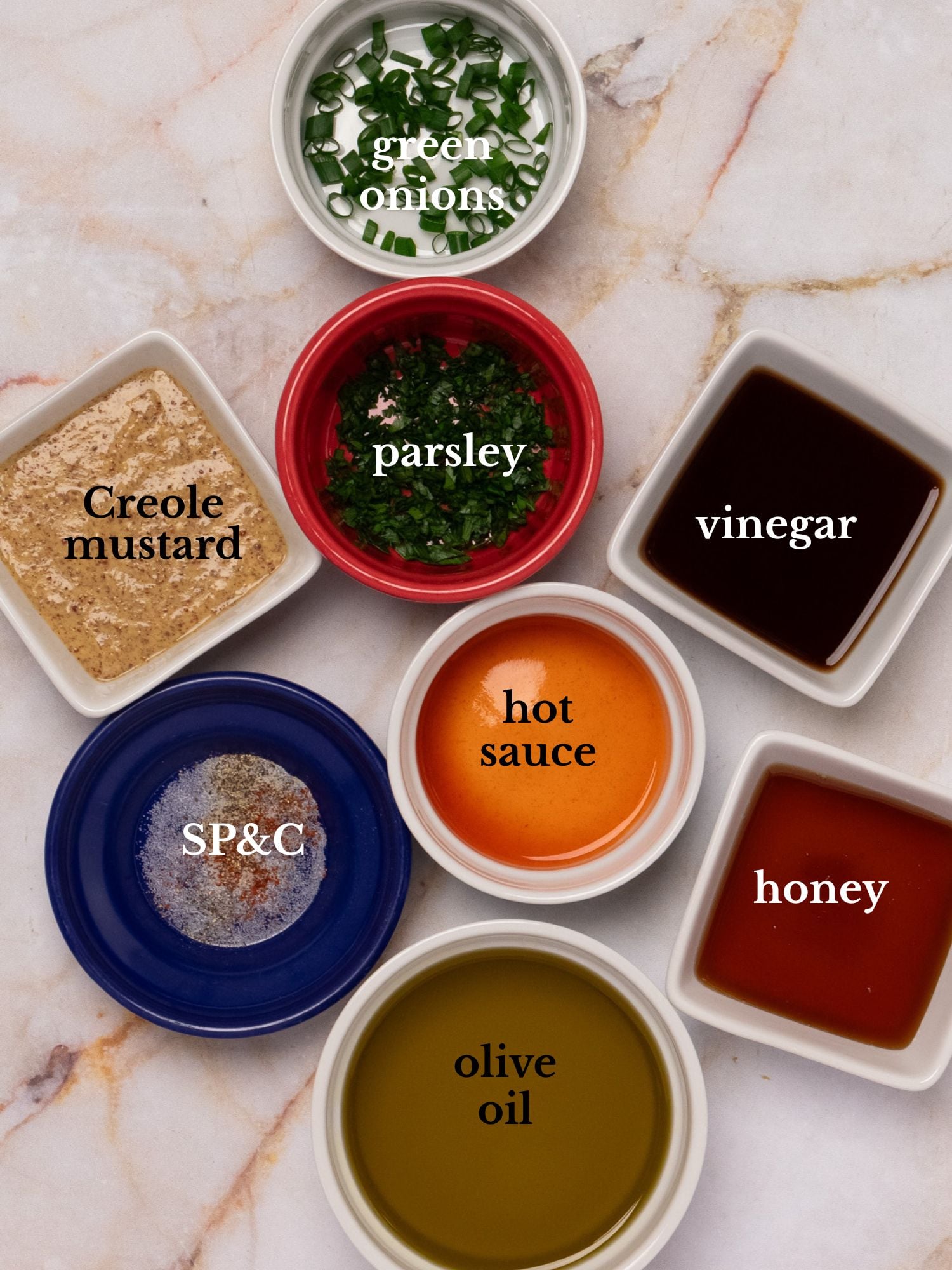Ingredients for Creole mustard vinaigrette in bowls on a white marbled background.