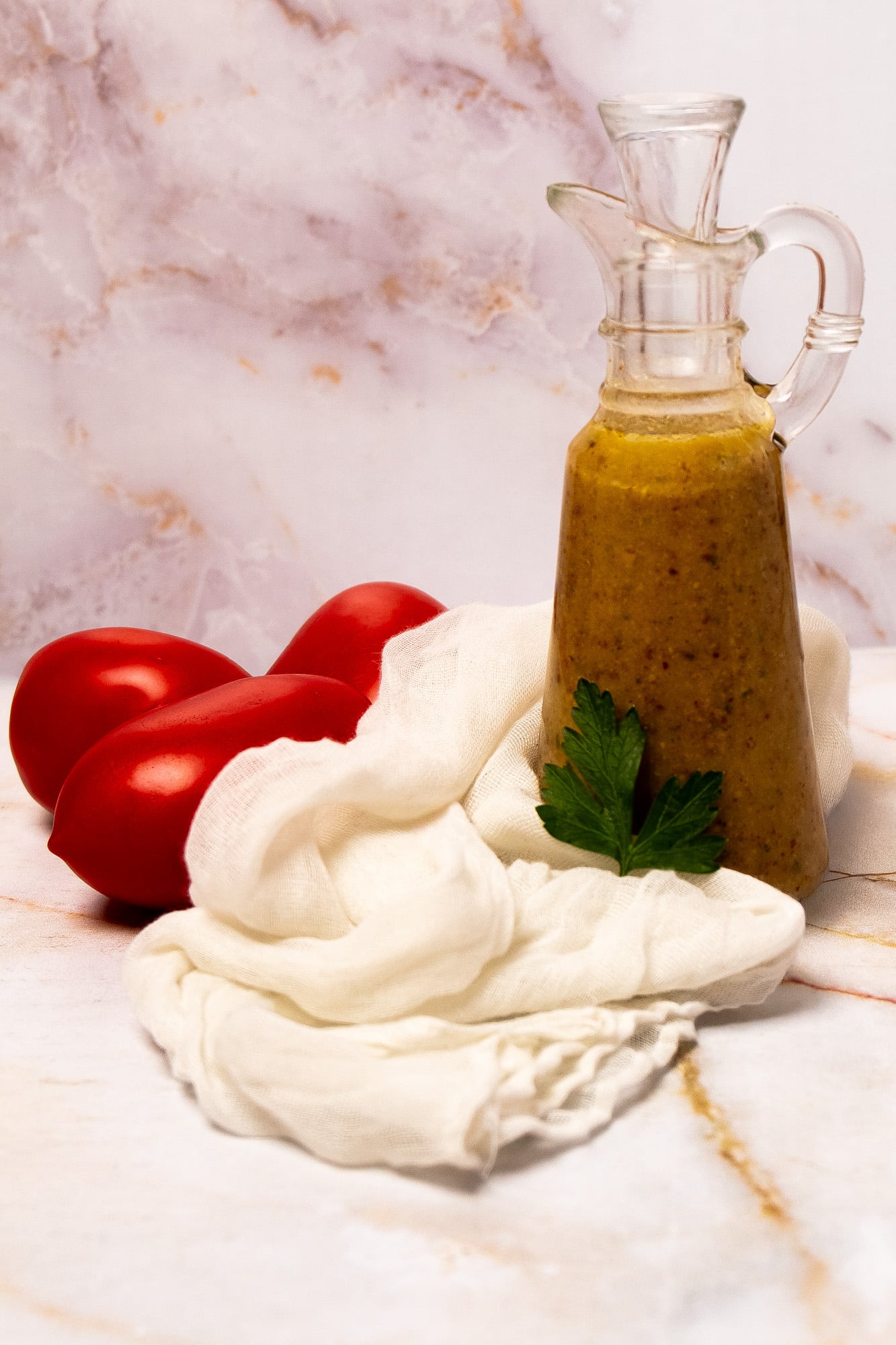 Creole mustard vinaigrette in a glass salad dressing jar with a whole parsley leaf in front of it and a white linen napkin and three tomatoes on the left side.