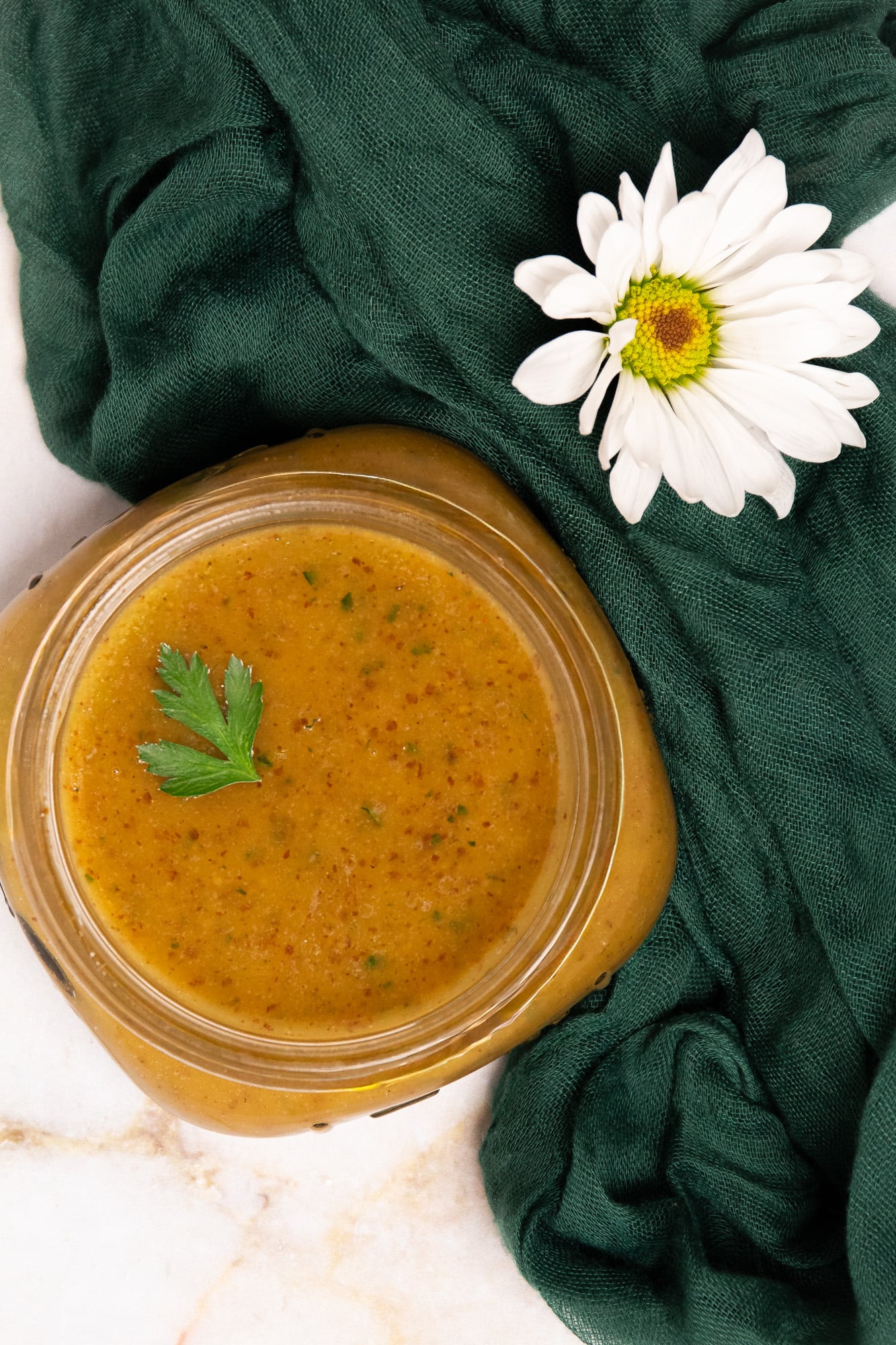 Creole mustard vinaigrette in a small clear Mason jar with a whole parsley leaf garnish alongside a dark green linen napkin and white daisy flower.