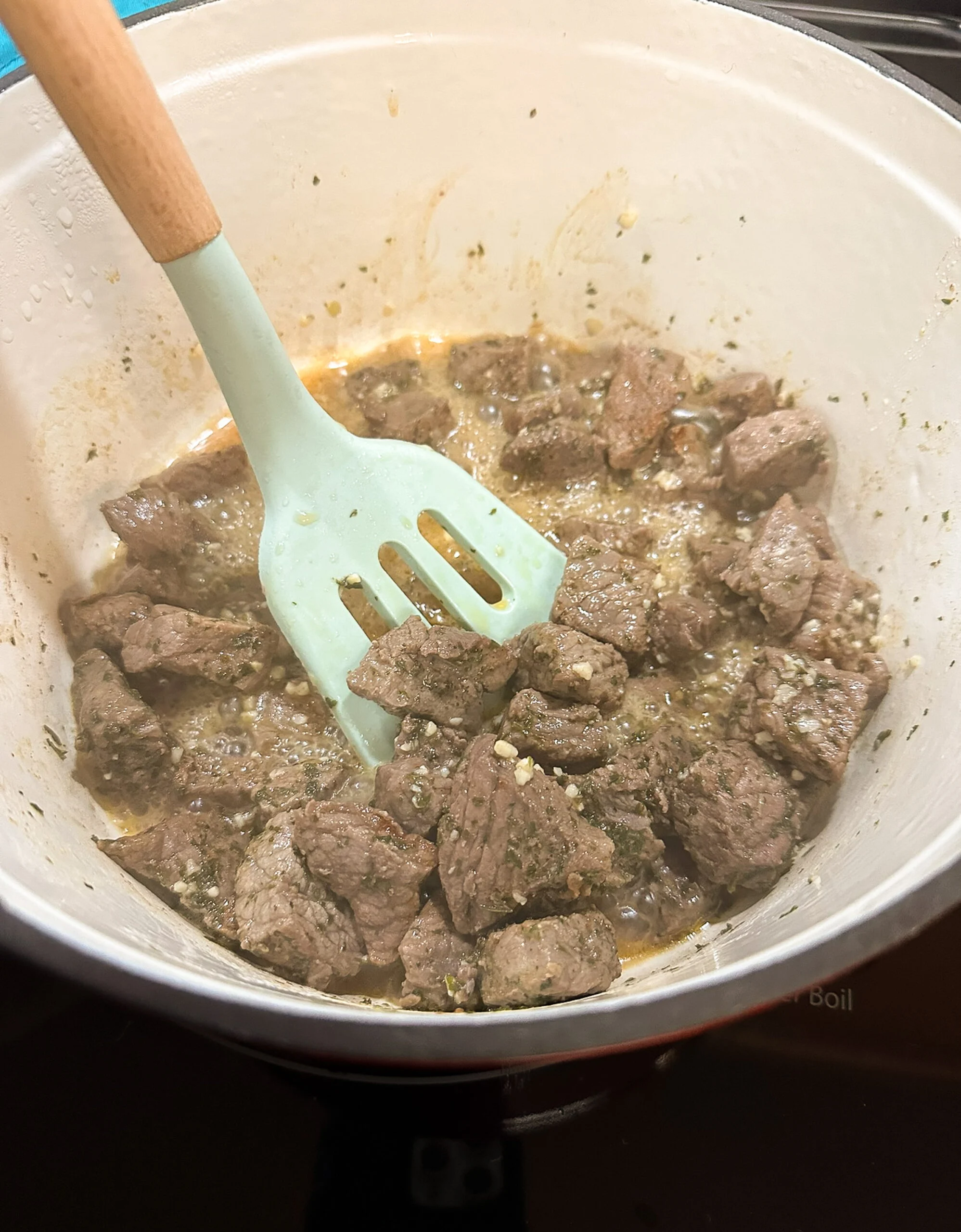 A slotted spatula removing browned beef and garlic out of a pot.