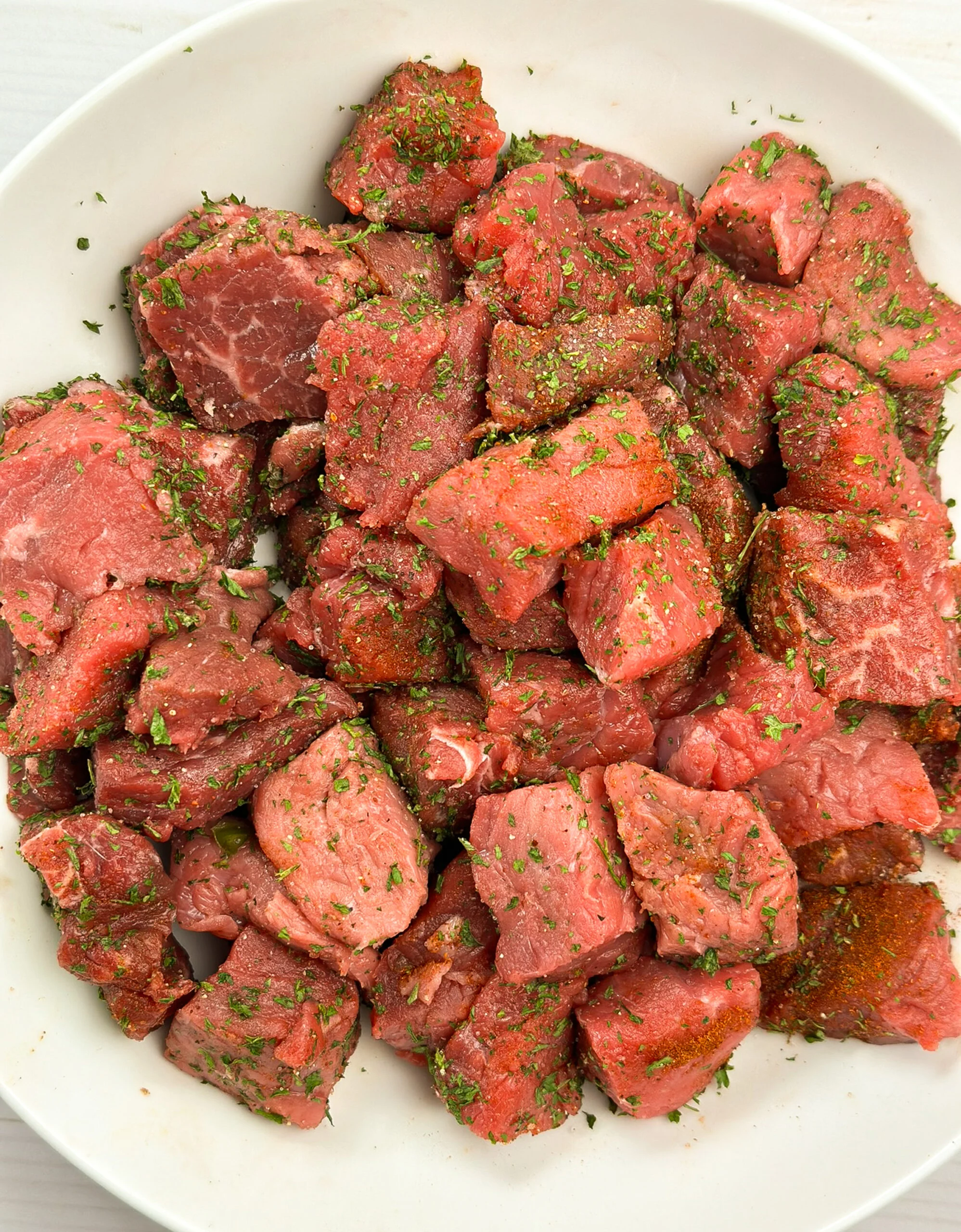 Raw seasoned chopped top round steak pieces in a white bowl.
