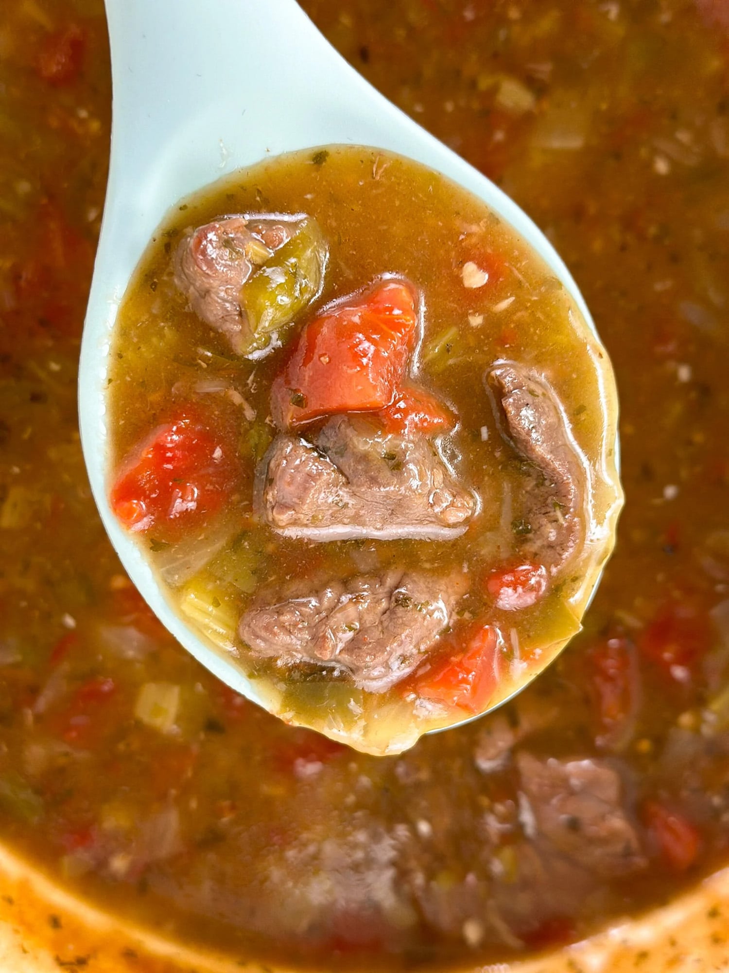 Grillades and grits in a serving spoon over a pot.