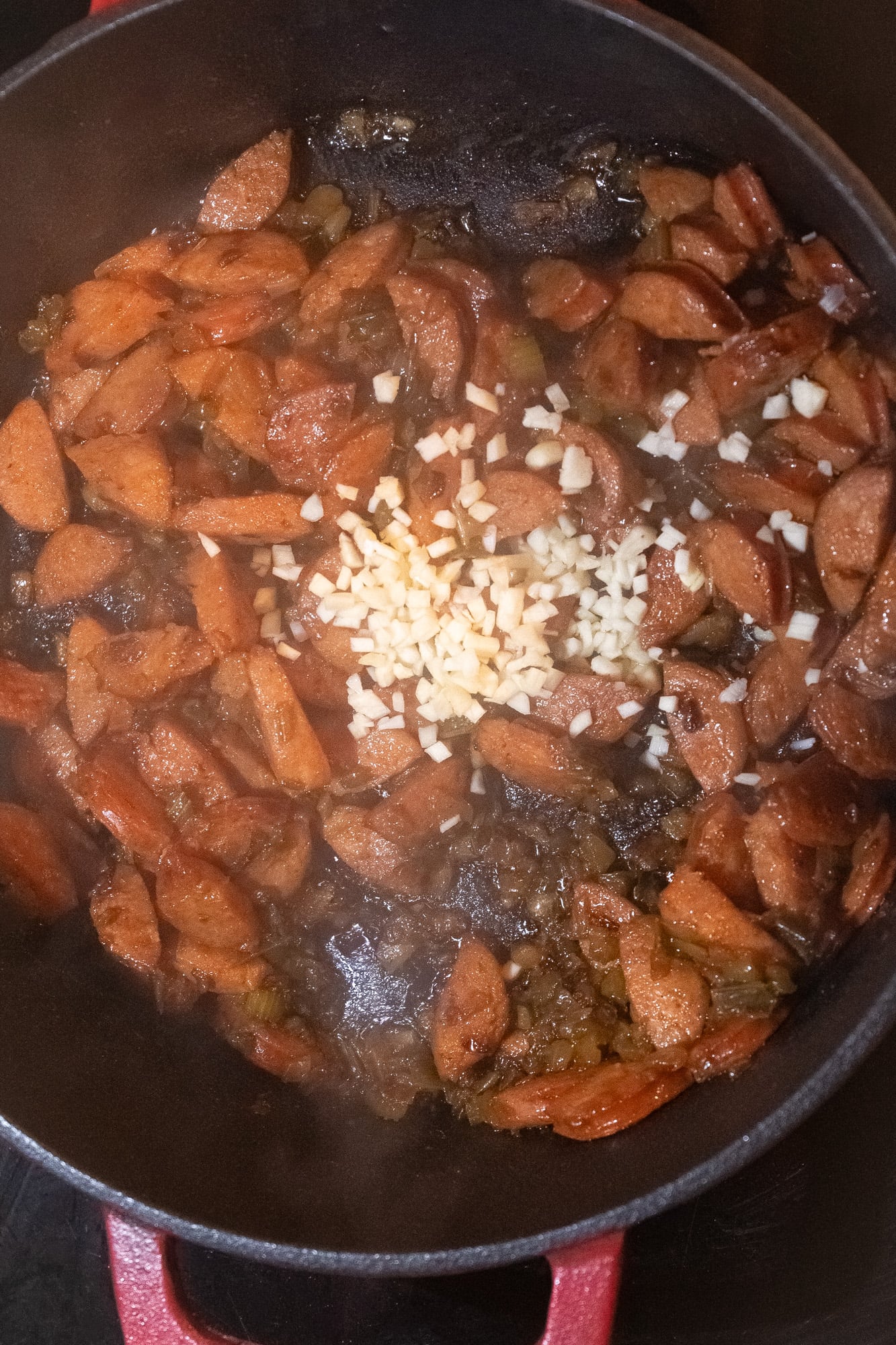 Minced garlic, and browned vegetables and sliced smoked sausage in a Dutch oven on the stove.