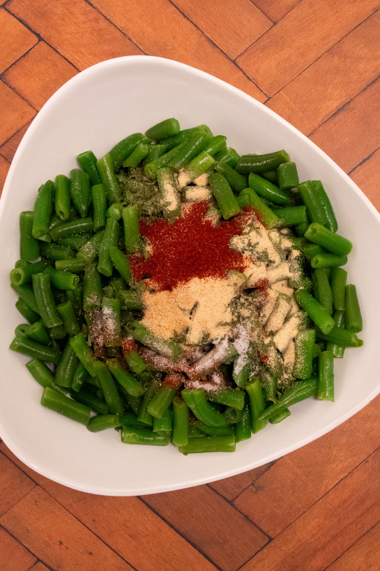 Cut green beans in a white bowl with dried seasonings on top.
