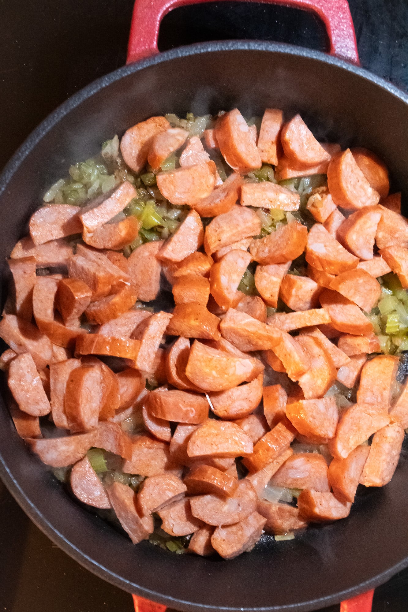 Browned chopped vegetables with sliced smoked sausage in a pot.