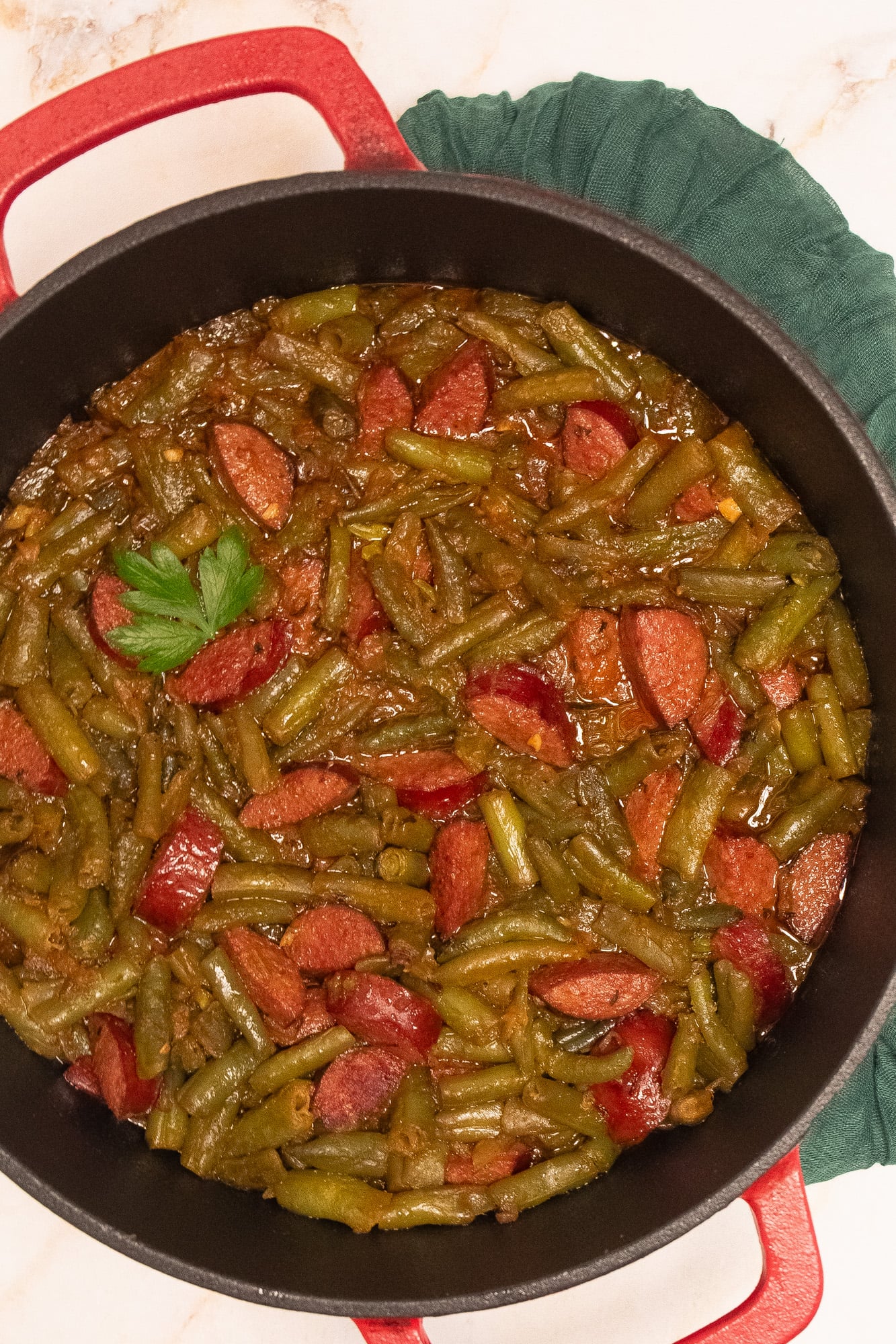 Cajun smothered green beans in a red enameled cast iron Dutch oven.