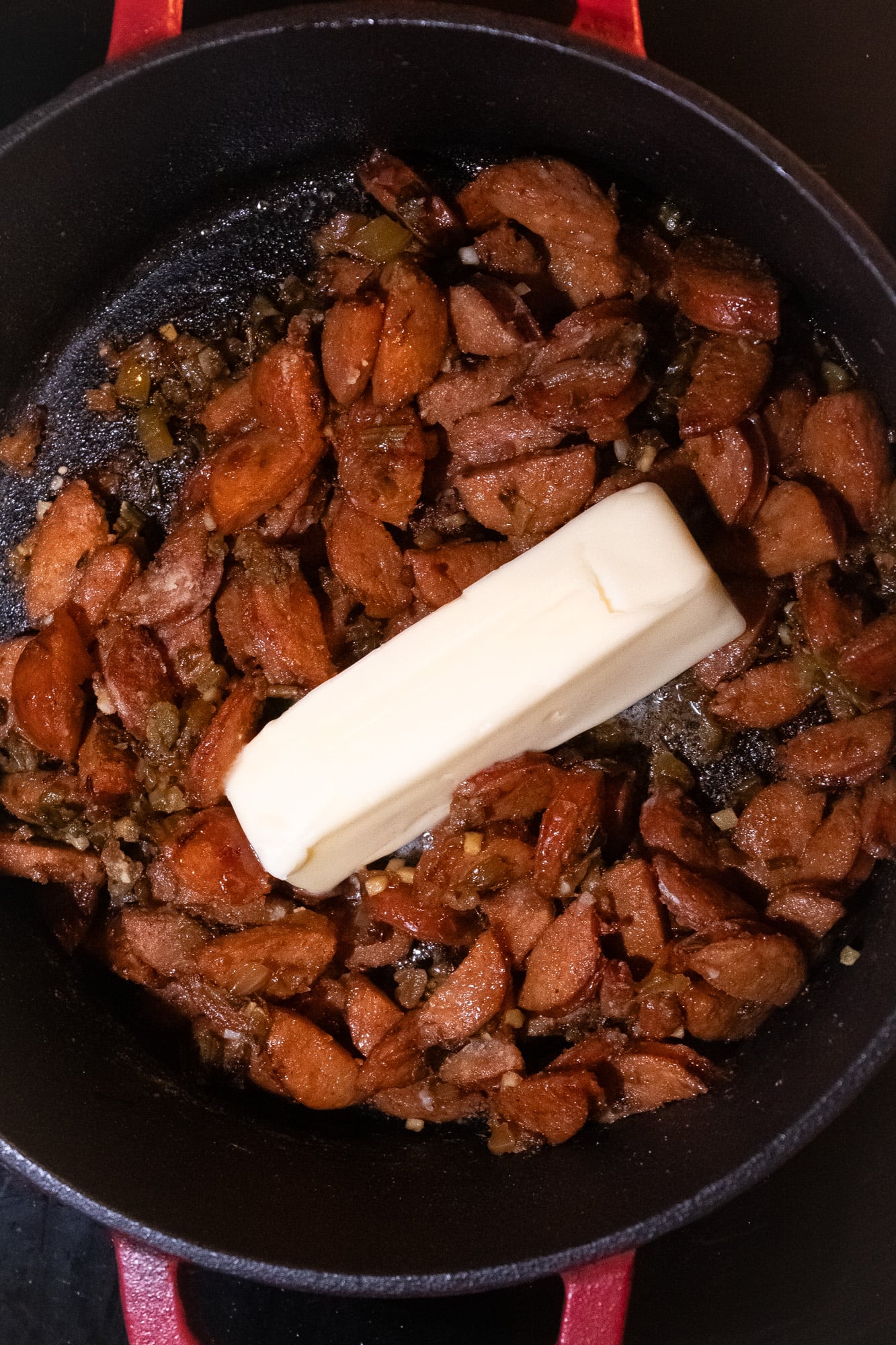 A stick of butter on top of browned meat and vegetables in a pot.